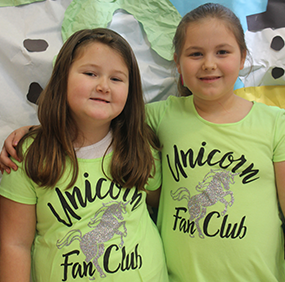 Two smiling female students pose together wearing shirts that say Unicorn Fan Club