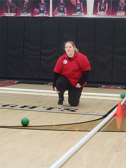 Player in red watching green bocce ball