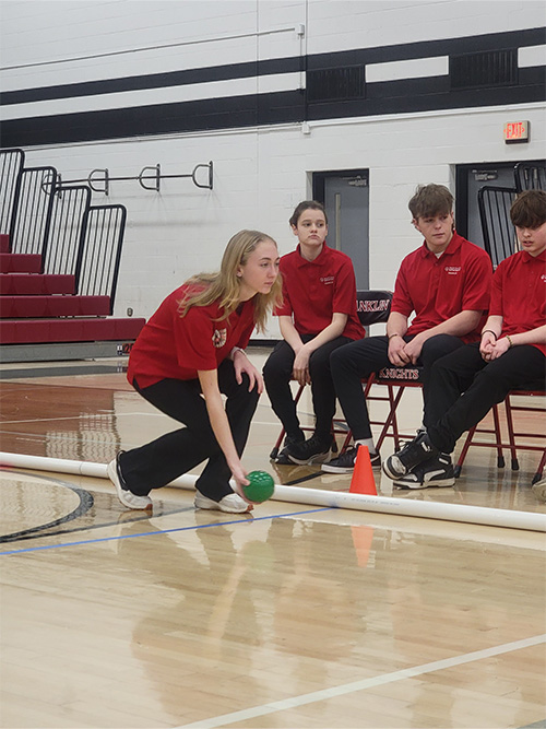 Teammates watch as player rolls the green ball