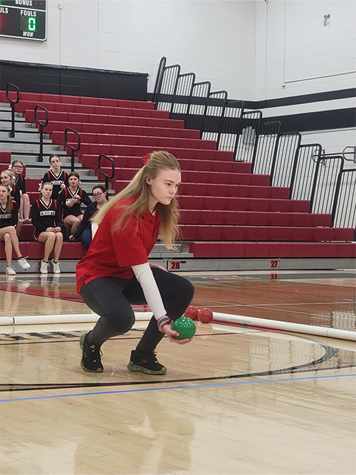 Girl kneeling on the court preparing to roll the green ball